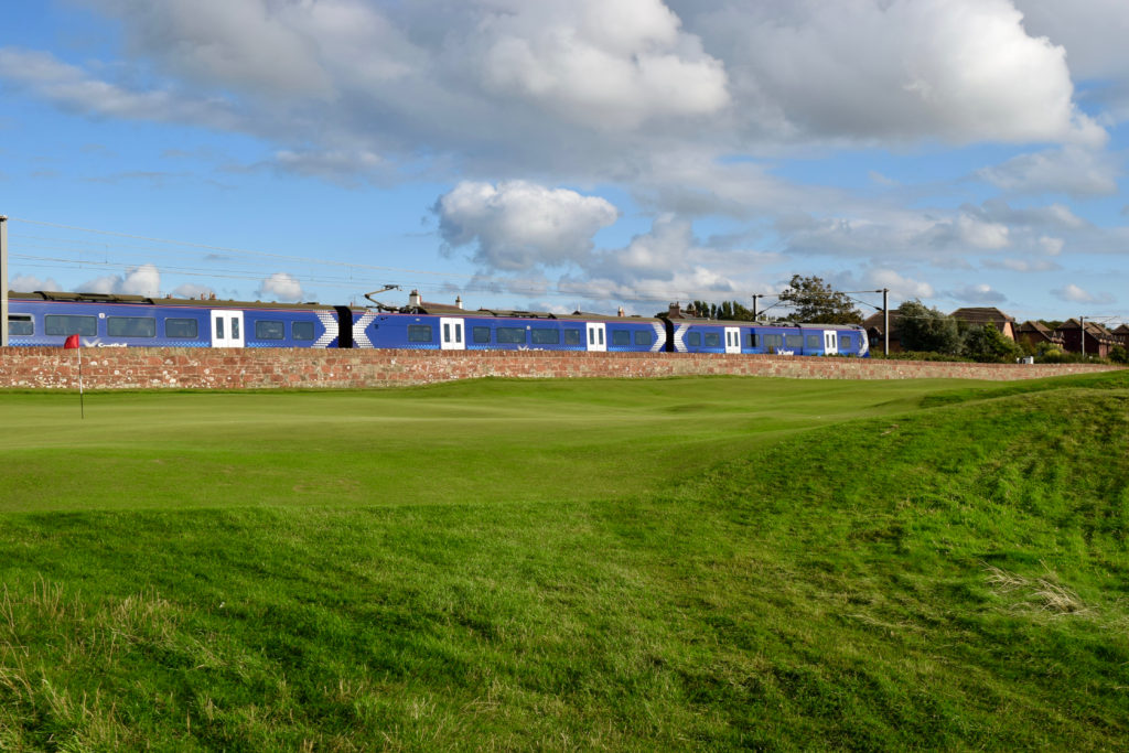 A train roars by the green and fairway on the first hole at Prestwick Golf Club in Scotland.